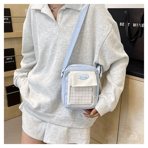 Détail du sac bandoulière en toile bleu et blanc avec écusson et garniture à carreaux