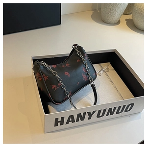 Detail view of black printed handbag with red floral patterns and silver chain strap