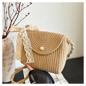 Close-up of a straw shoulder bag featuring a large pearl clasp and delicate lace bow detail