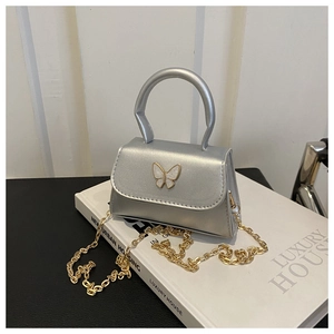 Detailed close-up of silver mini handbag featuring a white butterfly ornament and gold chain