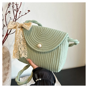Detail of light green straw bag with white pearl accent and lace bow on a textured weave