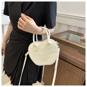 Detail of white apple-shaped handbag featuring crocodile texture and dual top handles