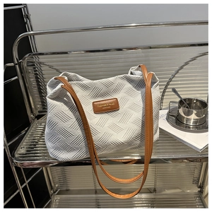 Detail of white woven tote bag with brown straps and embossed leather brand patch