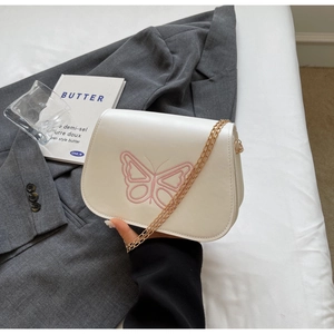 Détail d'un sac bandoulière élégant en cuir crème avec broderie papillon et chaîne dorée