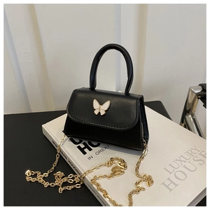 Detail of black mini crossbody bag with white butterfly buckle on a luxury prop book
