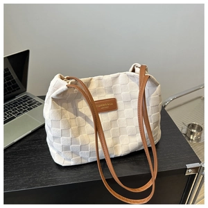 Detail of woven tote bag with brown leather handles and central fashion brand patch