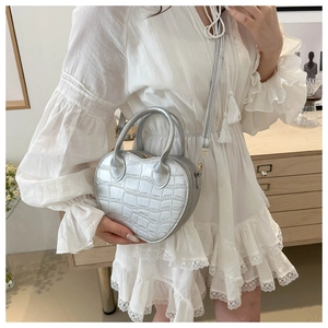 Detail of silver heart-shaped handbag with crocodile texture shown on female model
