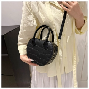 Detail of black heart-shaped handbag featuring crocodile texture and gold hardware