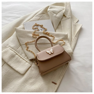 Close-up of elegant bow-shaped metal clasp and golden chain on a beige leather handbag