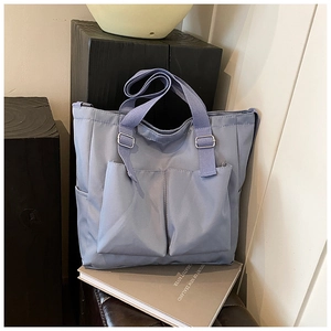 Detail of grey-blue nylon tote bag featuring dual front pockets and adjustable strap