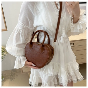 Close-up of brown heart-shaped crossbody bag with crocodile texture and double handles