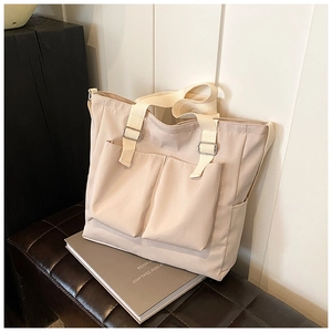 Close-up of beige Oxford cloth tote bag featuring large front pockets and woven straps