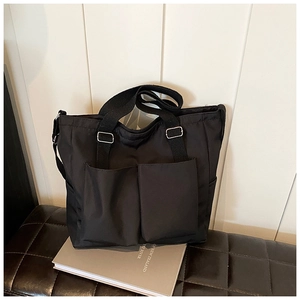 Detail of black nylon tote bag featuring front pockets and silver metal buckle