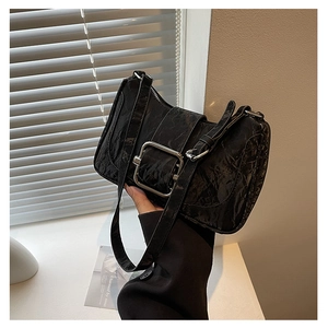 Detail of black glossy wrinkled leather texture and silver rectangular buckle on handbag