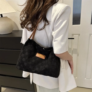 Black woven tote bag with brown leather straps shown on shoulder in minimalist interior