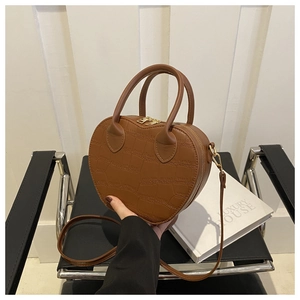 Detail of caramel brown heart-shaped bag with crocodile pattern and golden hardware