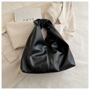 Close-up of black pleated PU leather hobo bag on a beige blazer and book
