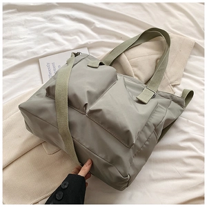 Detail of grey-green nylon tote bag with large pockets and wide shoulder straps on white linen