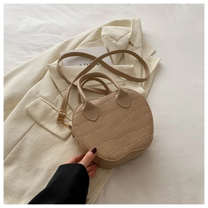 Detail of beige crocodile embossed handbag with gold hardware and round handle
