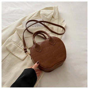 Close-up of brown apple-shaped handbag with crocodile texture on a white blazer