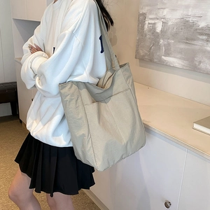 Minimalist beige tote bag with front pocket shown on shoulder in a lifestyle setting
