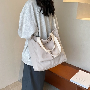 Light beige Oxford tote bag with dual front pockets shown on a model in a minimalist room
