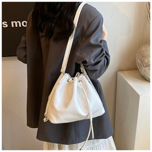 Detailed side view of white leather bucket bag with drawstring and shoulder strap on model