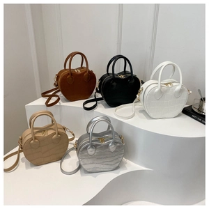 Detail showing various colors of crocodile pattern heart-shaped handbags on a white stand