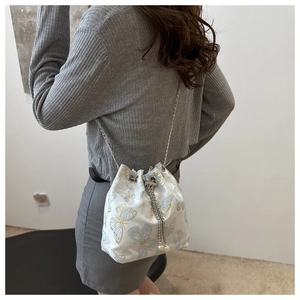 Detail of white satin bucket bag featuring blue butterfly embroidery and elegant tassels