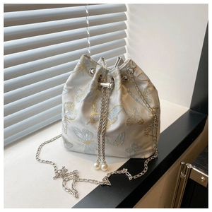 Detail of light blue bucket bag featuring embroidered butterfly and pearl drawstring