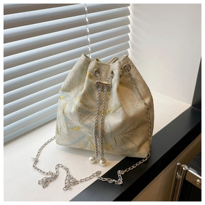 Detail of embroidered bucket bag with leaf pattern, metal chain and pearl drawstring