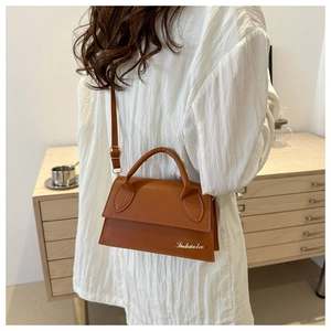 Brown faux leather mini bag featuring curved handle and metallic logo on wooden background