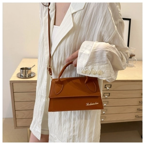 Detail of a mini orange trapezoid leather bag with gold logo and stylish metal hardware
