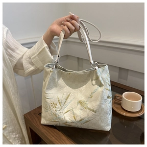 Detailed golden silk embroidery of birds and bamboo leaves on ivory shoulder bag