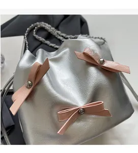 Détail du sac seau argenté avec nœuds en cuir rose et bandoulière en chaîne polie