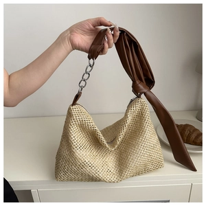 Detail of bohemian straw hobo bag featuring dark brown leather strap and silver chain link