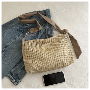 Detail of woven straw tote bag featuring brown leather strap and silver chain accents
