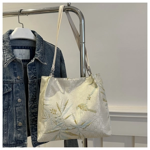 Detail of embroidered bamboo leaves and birds on a beige canvas tote bag with golden thread
