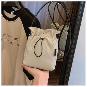 Detail of minimalist beige nylon crossbody bag with drawstring closure and fashion tag