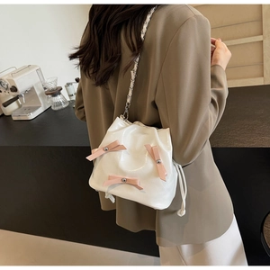 Détail du sac seau en cuir verni blanc avec nœuds roses et bandoulière sur modèle