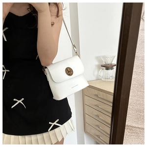 Detail view of a white vintage leather crossbody bag with an embossed round clasp and strap