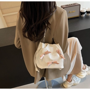 Détail du sac seau crème avec nœuds roses et bandoulière dans un décor de café moderne