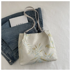 Detailed close-up of bamboo leaf embroidery on a cream shoulder bag with golden texture