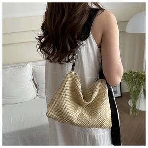Detail of woven straw tote bag featuring black leather strap and silver chain handle