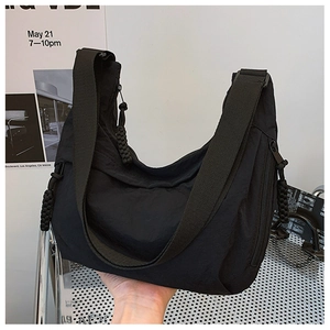 Detail of black nylon dumpling bag featuring woven rope zipper and wide shoulder strap