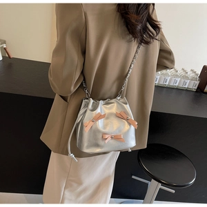 Détail d'un sac seau argenté avec des nœuds roses en 3D et une bandoulière en chaîne