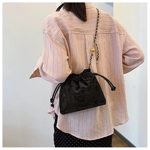 Détail du sac seau noir avec bandoulière chaîne et perle dorée porté par un modèle