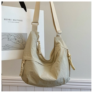 Detail of minimalist beige nylon crossbody bag featuring a braided rope zipper charm