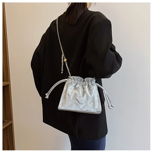 Détail du sac seau matelassé argenté avec bandoulière chaîne sur blazer noir