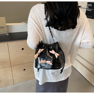 Vue détaillée du sac seau noir brillant avec nœuds roses et bandoulière en chaîne